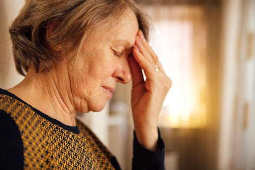 Senior woman holding her head in distress, experiencing a headache, a common symptom of brain fog during menopause, linked to hormonal changes and cognitive decline.