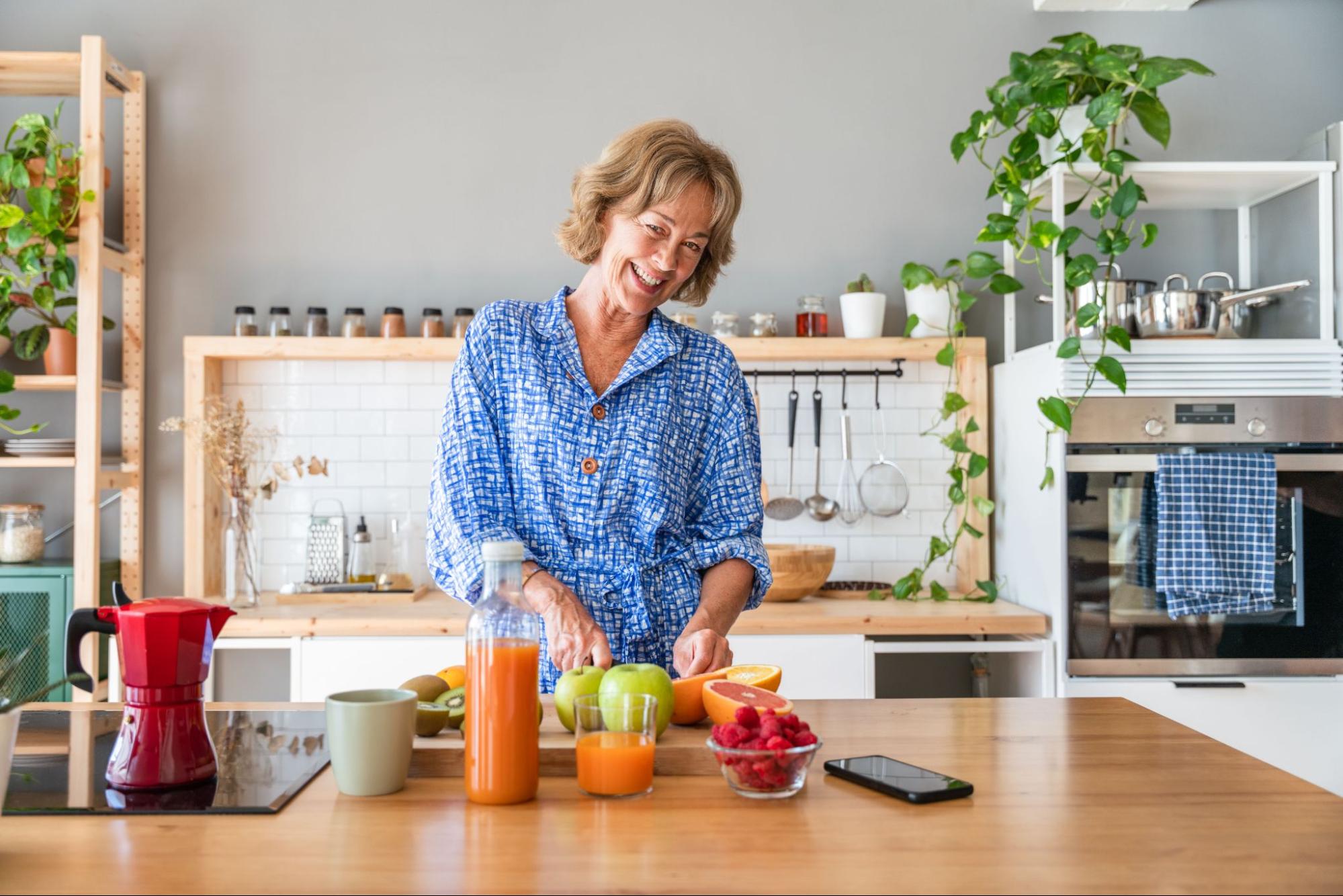 Woman preparing fresh fruit and juice in a home kitchen, supporting healthy nutrition during menopause.