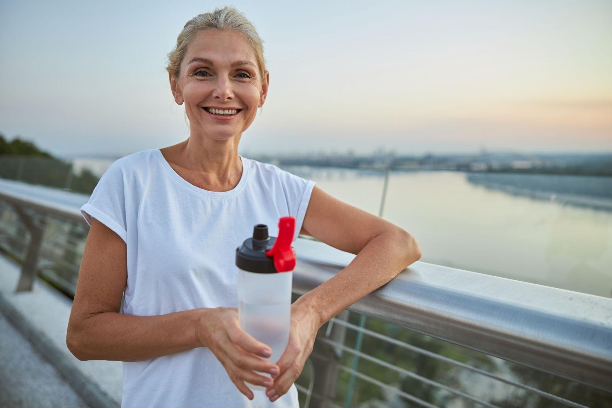 Woman holding a water bottle outdoors after exercise, supporting hydration and fitness during menopause.
