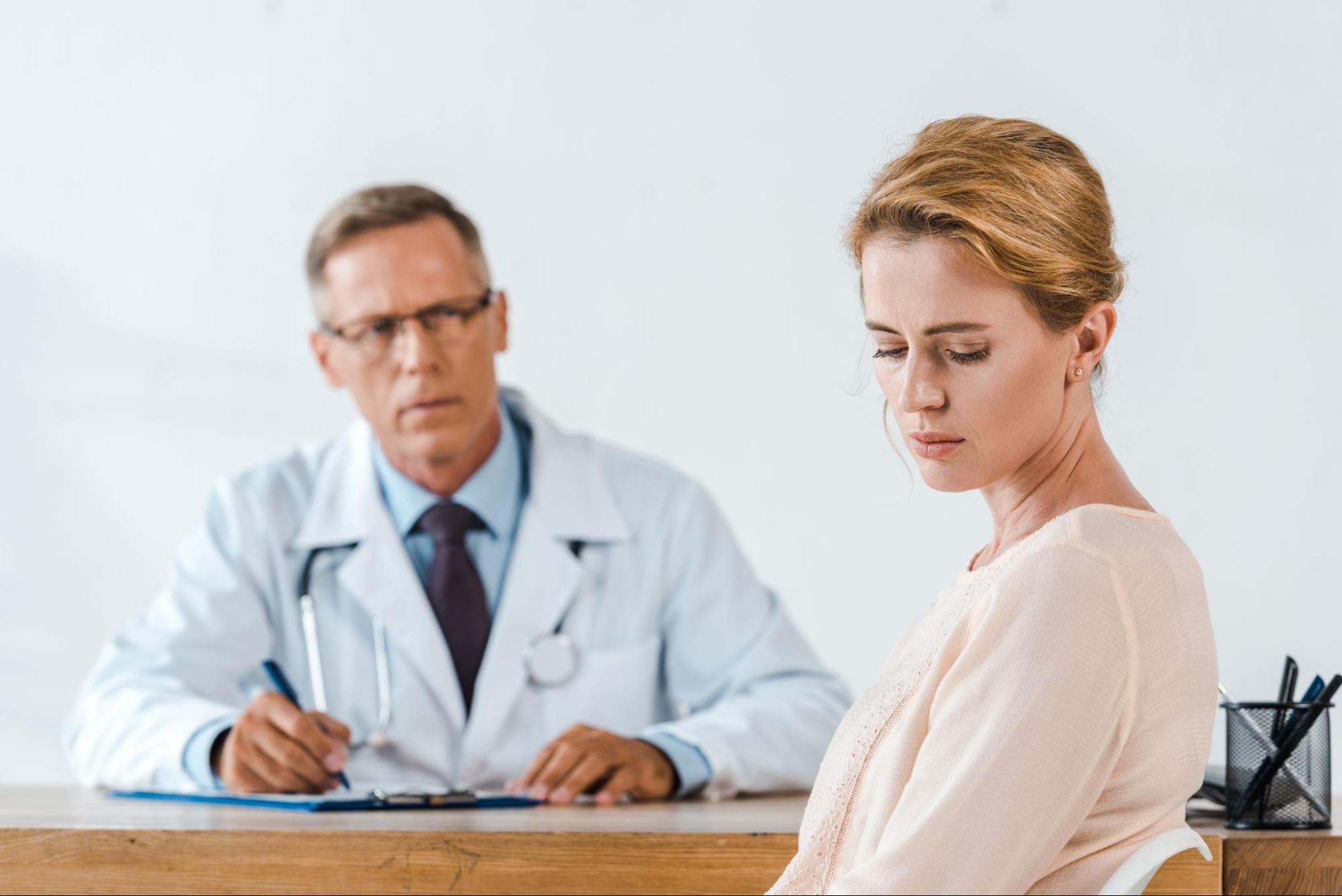 Woman appearing distressed during a medical consultation with a doctor, representing concerns about menopause symptoms and feeling dismissed in healthcare.